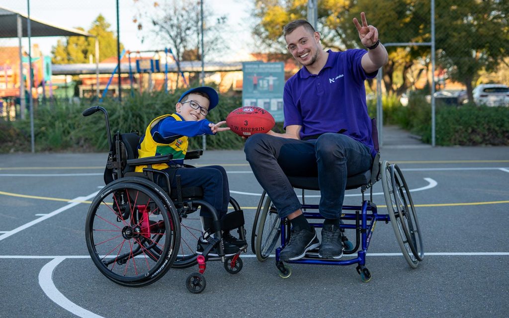 Young boy and man in wheelchairs, with the man holding a football